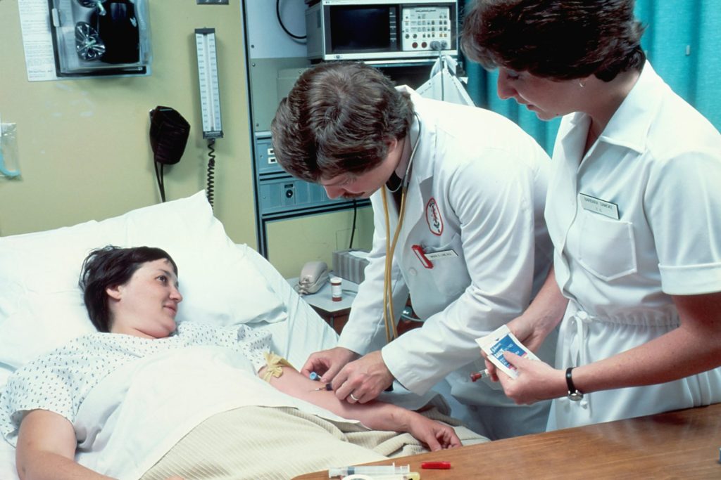 Eine Frau liegt in einem Krankenhausbett neben einem Mann.